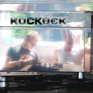 Cover Kuckuck (album) - the two ACF protagonists inside a cafe in Witzenhausen, bright sunlight shining through the window onto them reading, from the back.